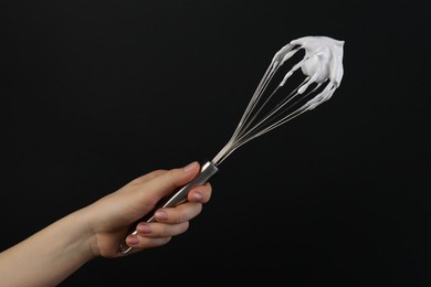 Woman holding whisk with whipped cream on black background, closeup