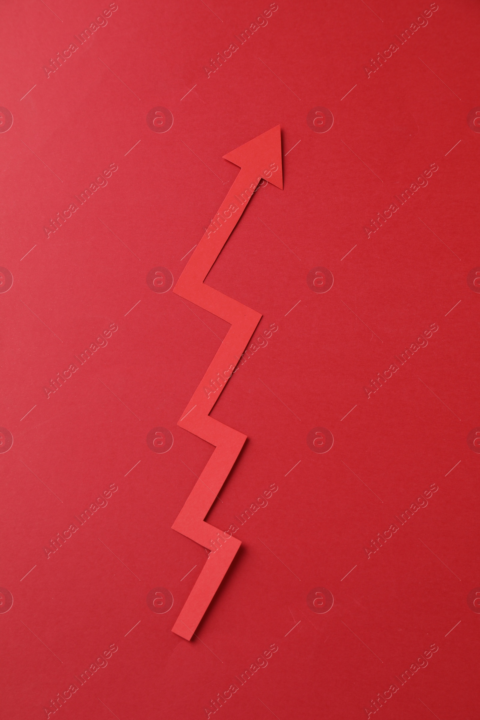 Photo of One zigzag paper arrow on red background, top view