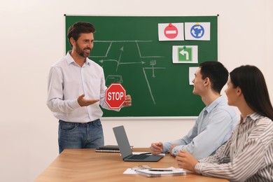 Photo of Teacher showing Stop road sign to audience during lesson in driving school