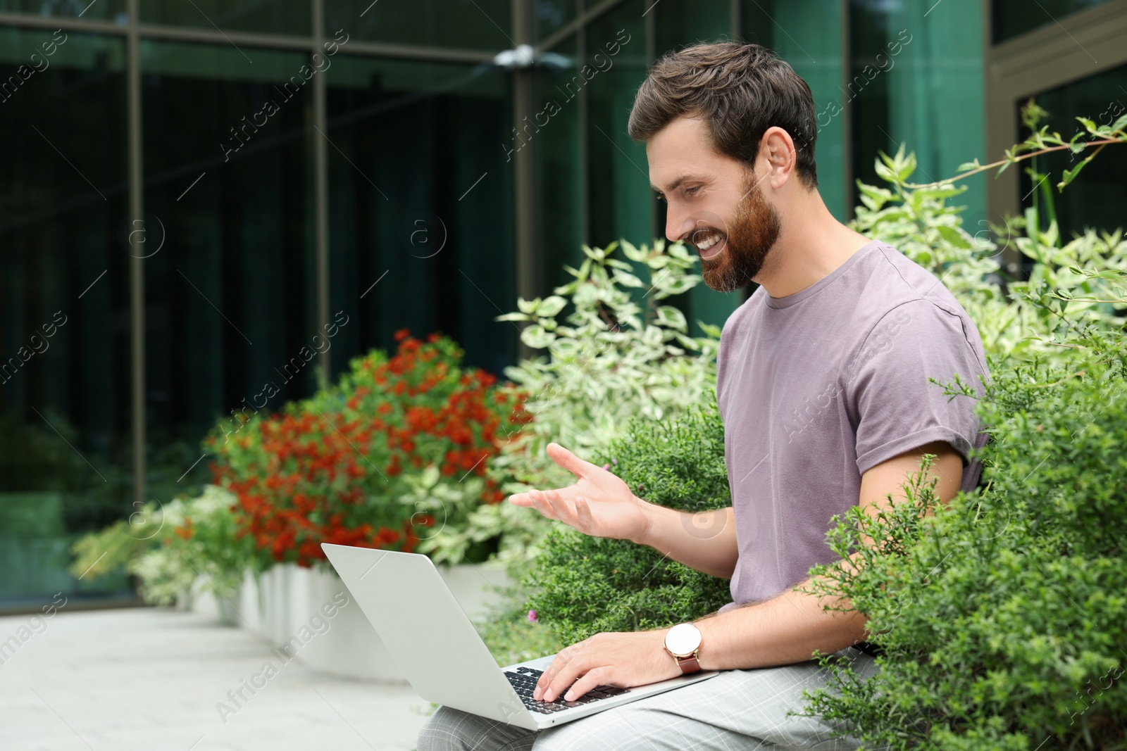 Photo of Handsome man with laptop near beautiful plants on city street