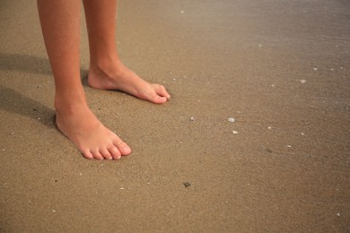 Little girl standing on sandy beach near sea, closeup. Space for text