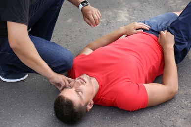 Photo of Passerby checking pulse of unconscious young man outdoors