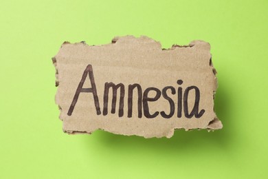 Photo of Piece of cardboard with word Amnesia on light green background, top view