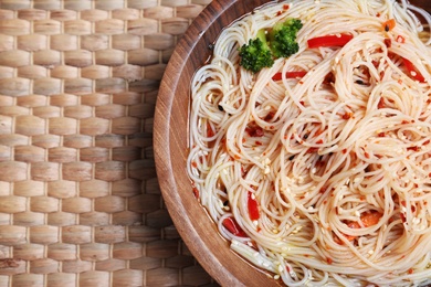Photo of Bowl of delicious noodles with broth and vegetables on wicker background, top view. Space for text