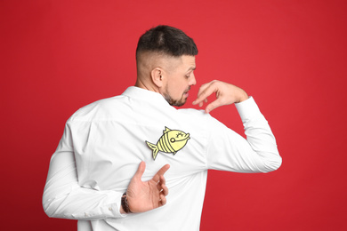 Man with paper fish on back against red background. April fool's day