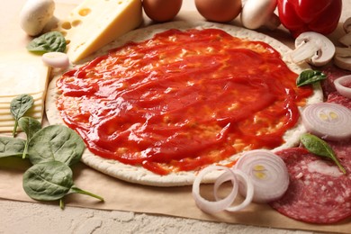 Photo of Pizza base smeared with tomato sauce and products on light textured table, closeup