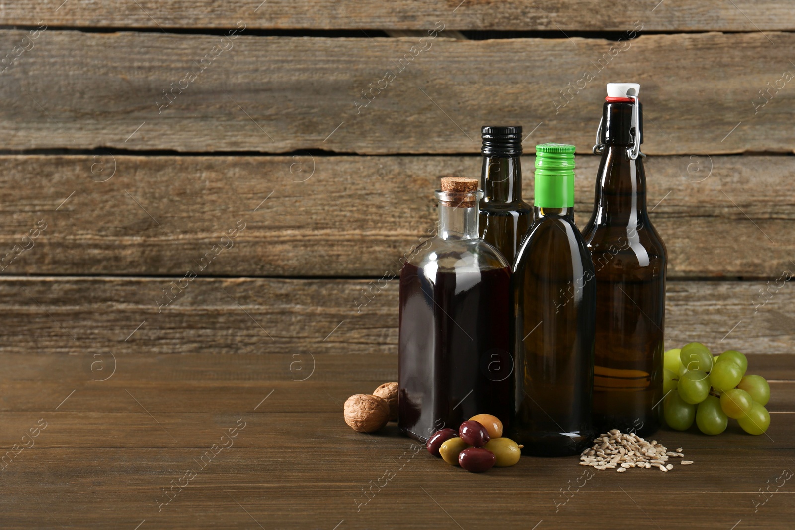 Photo of Vegetable fats. Different cooking oils in glass bottles and ingredients on wooden table, space for text