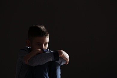 Upset boy on dark background. Space for text