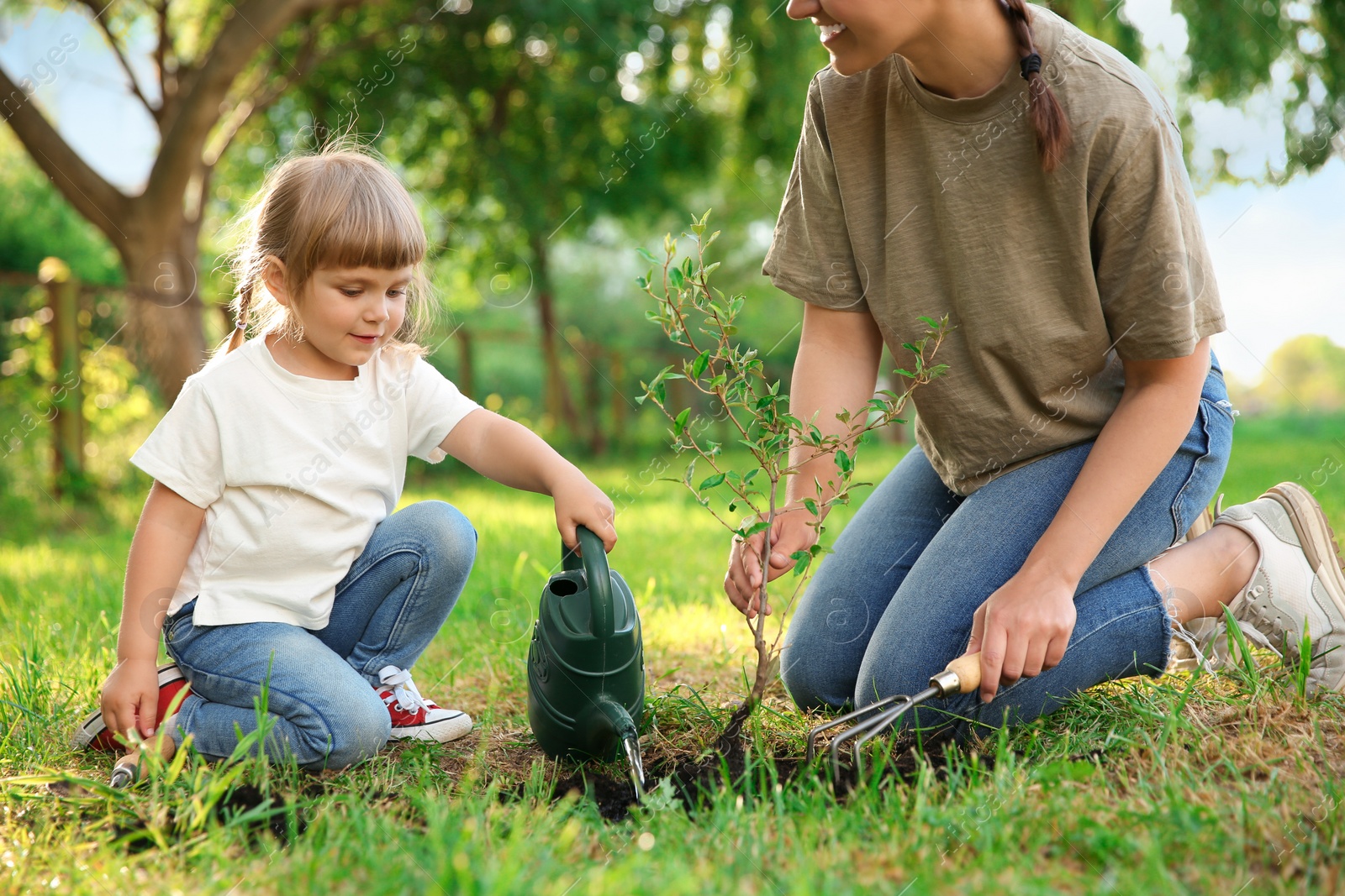 Photo of Mother and her daughter planting tree together in garden