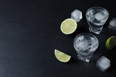 Shot glasses of vodka with lime slices and ice on black table. Space for text
