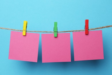 Photo of Wooden clothespins with blank notepapers on twine against light blue background. Space for text