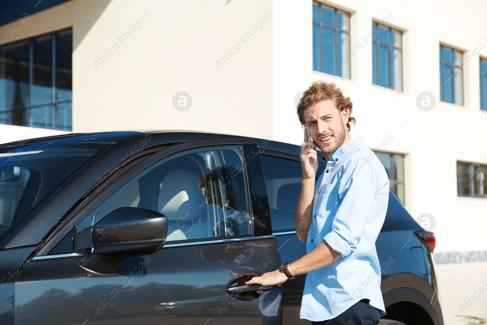 Photo of Young man talking on phone while opening car door, outdoors