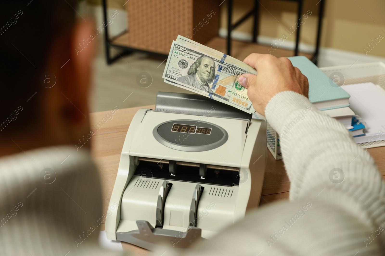 Photo of Man putting money into banknote counter at wooden table indoors, closeup