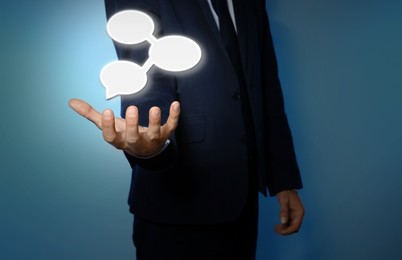 Communication and dialogue concept. Businessman with illustration of speech bubbles on light blue background, closeup