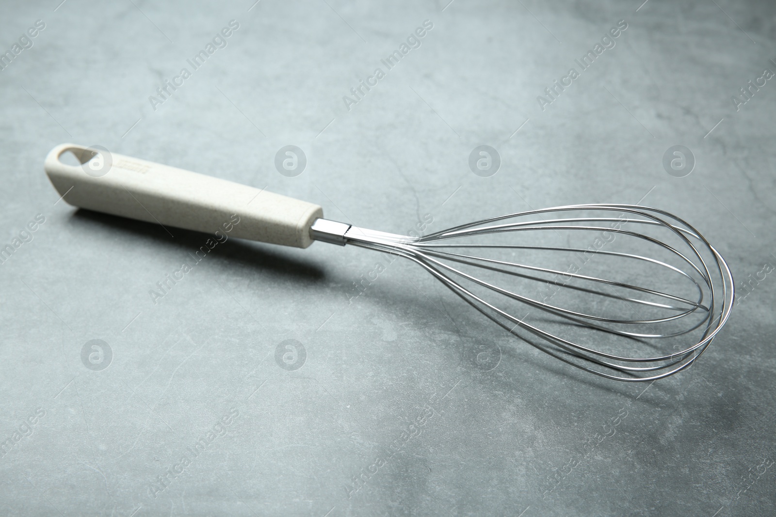 Photo of Metal whisk on gray table. Kitchen tool