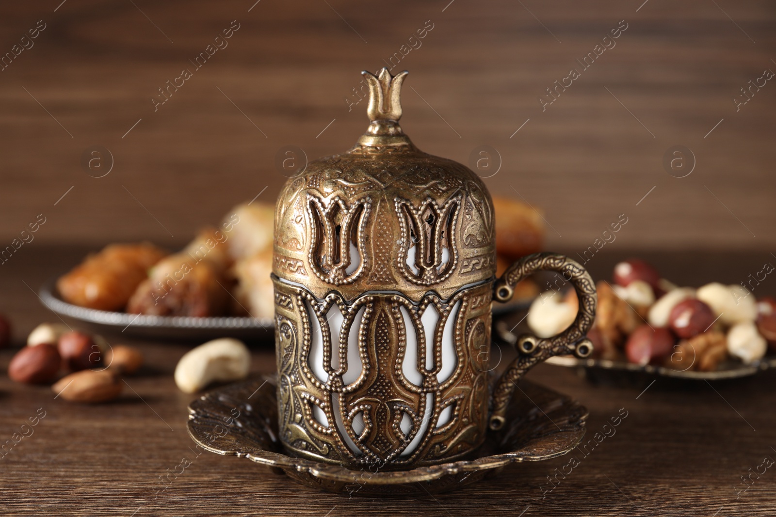 Photo of Beautiful cup holder, nuts and baklava dessert on wooden table, closeup