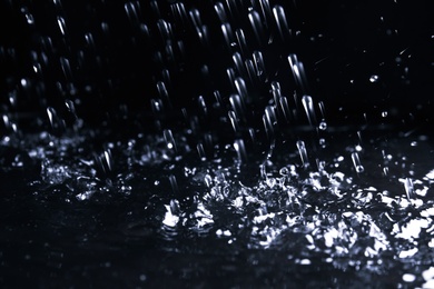 Photo of Heavy rain falling down on ground against dark background, closeup