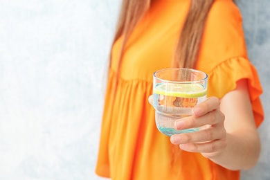 Young woman holding glass of lemon water on color background, closeup