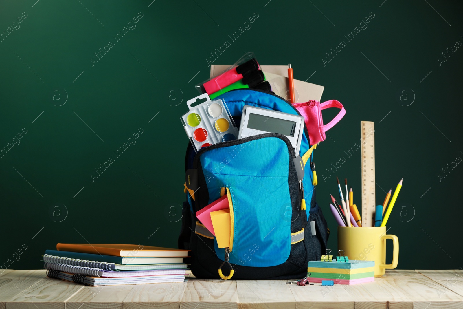 Photo of Backpack with different school stationery on white wooden table near chalkboard