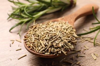 Spoon with dry rosemary on wooden table, closeup