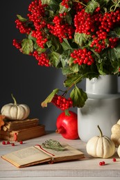 Photo of Composition with ripe red viburnum berries, books and pumpkins on table. Cozy autumn atmosphere