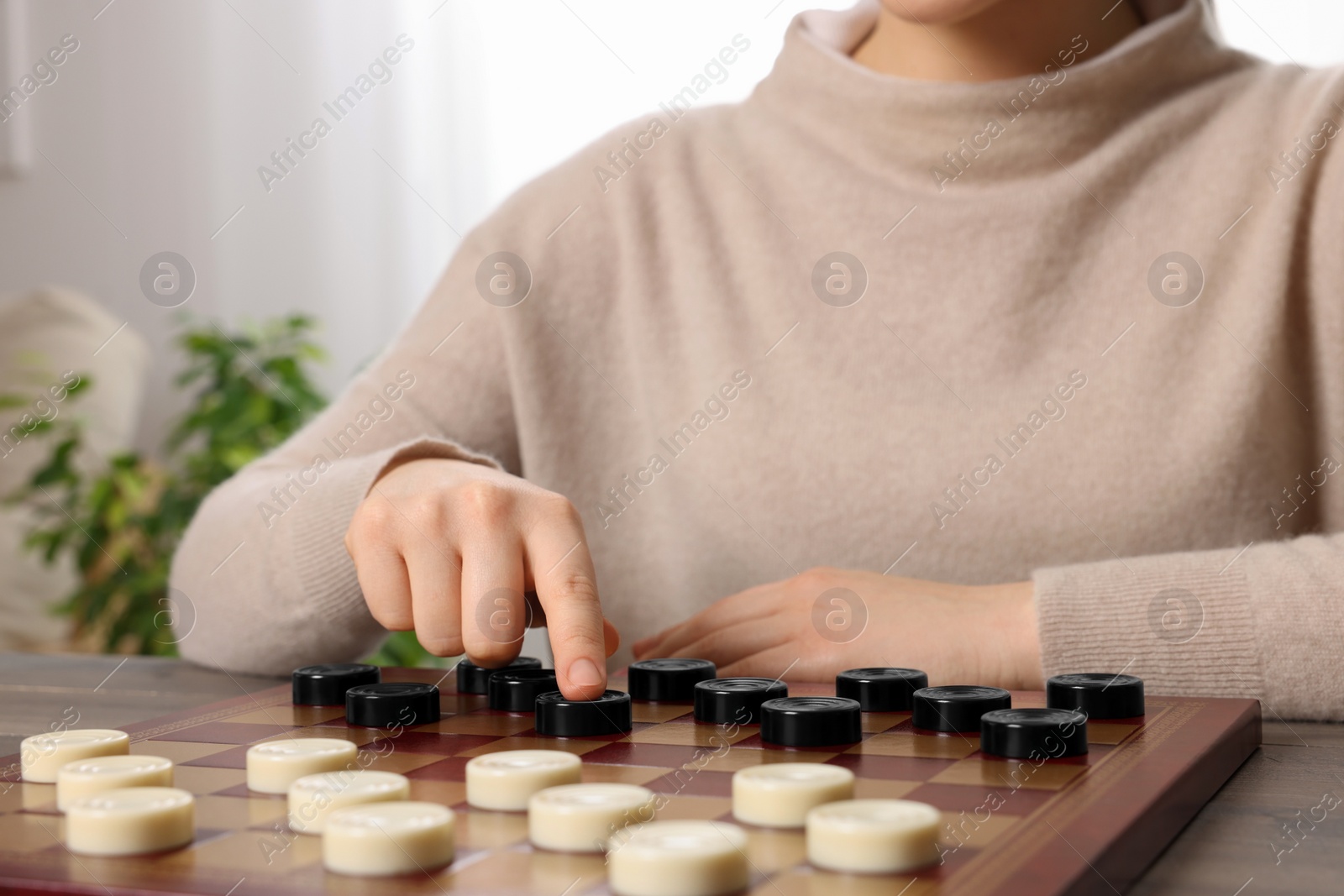 Photo of Playing checkers. Woman thinking about next move at table in room, closeup