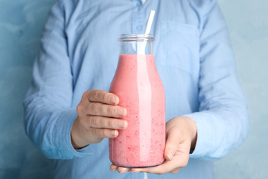 Woman holding tasty strawberry smoothie on light blue background, closeup