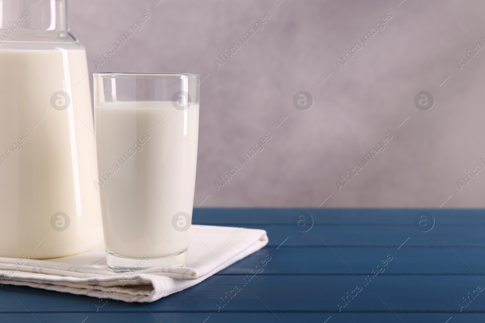 Photo of Carafe and glass of fresh milk on blue wooden table, space for text