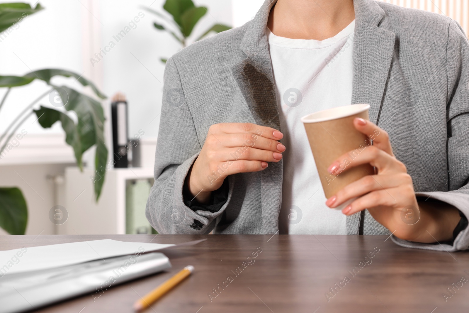 Photo of Woman showing stain from coffee on her jacket at wooden table indoors, closeup