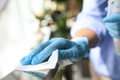 Woman in latex gloves cleaning railing with wet wipe indoors, closeup