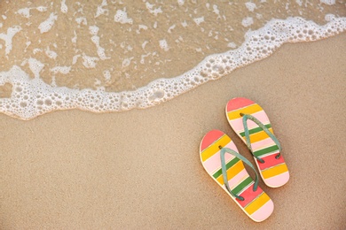 Stylish flip flops on sand near sea, top view with space for text. Beach accessories
