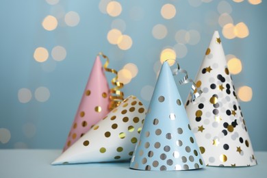 Photo of Beautiful party hats with streamers on light blue table against blurred festive lights. Space for text