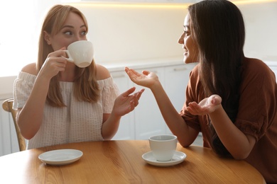 Photo of Young women talking while drinking tea at table in kitchen
