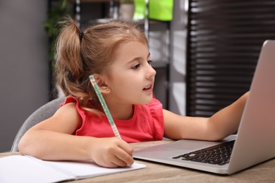 Photo of Cute little girl doing homework with laptop at table