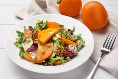 Photo of Delicious persimmon salad and fork on white wooden table