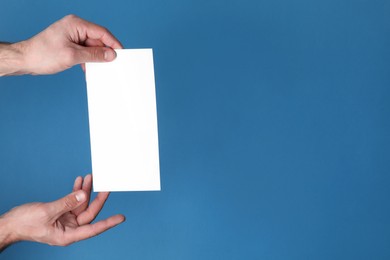 Man holding flyer on blue background, closeup. Mockup for design