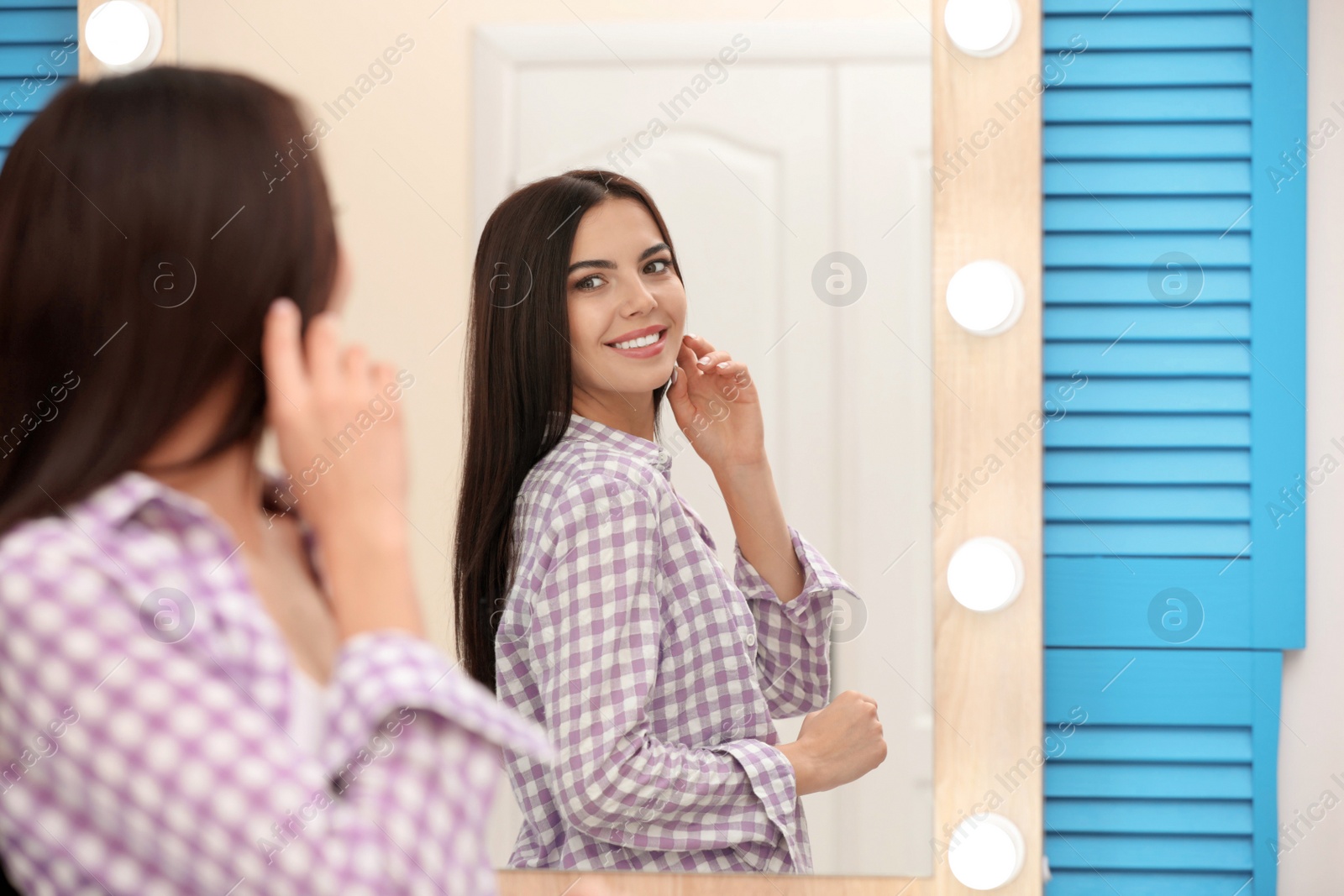 Photo of Young attractive woman looking at herself in stylish mirror at home