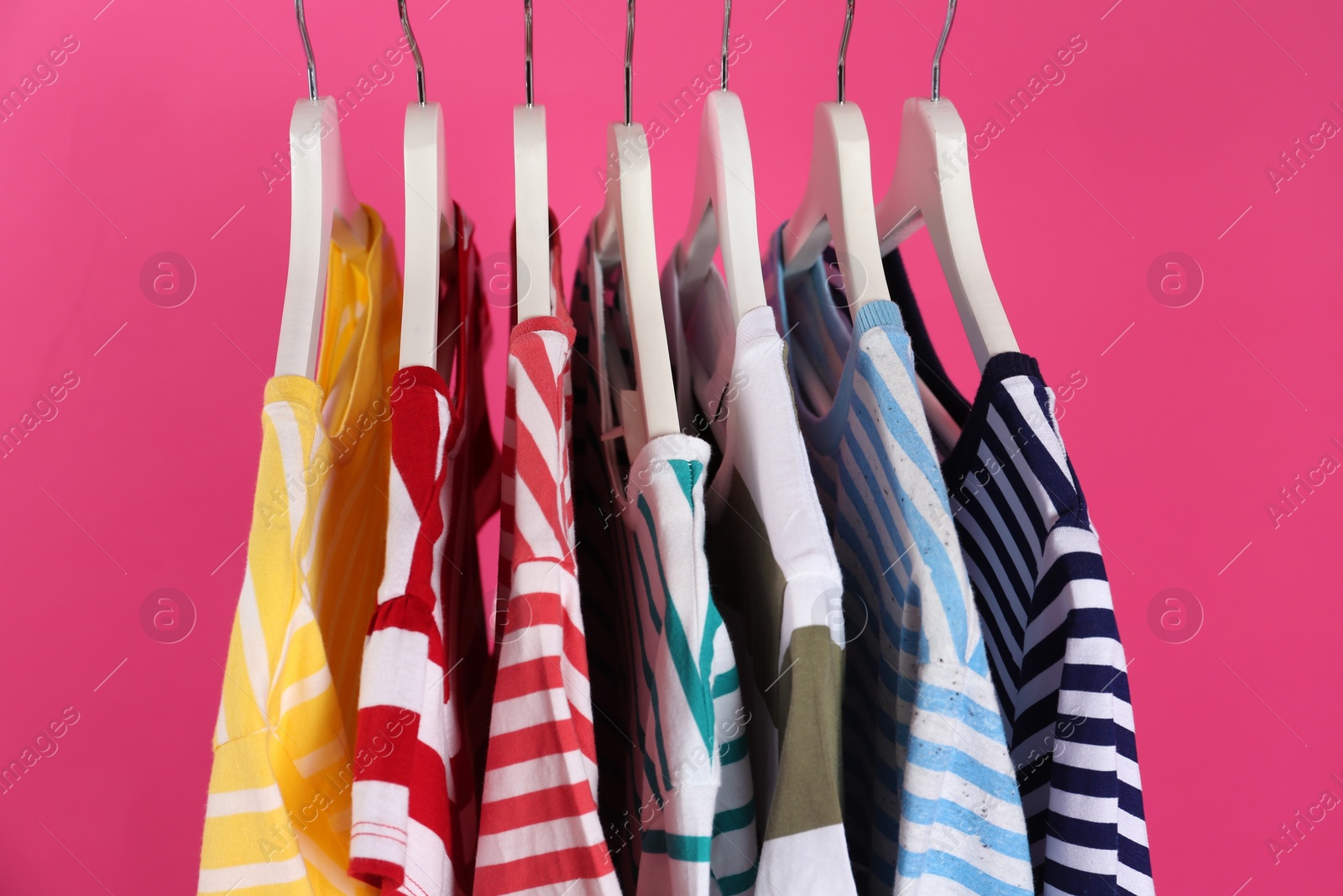 Photo of Colorful clothes on hangers against pink background