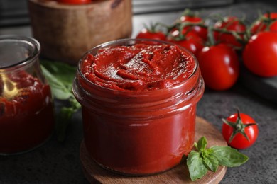 Photo of Jar of tasty tomato paste and ingredients on grey textured table, closeup