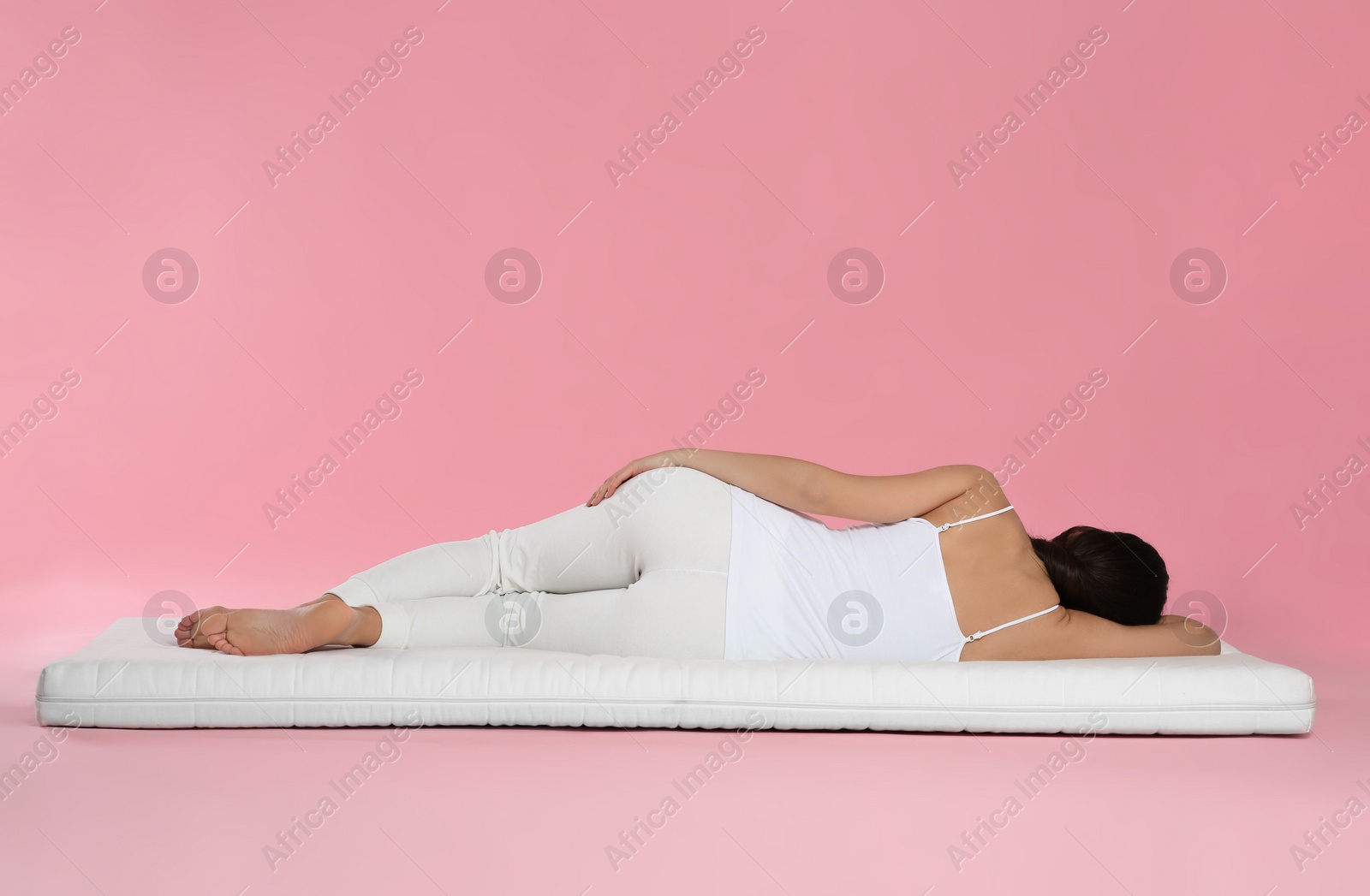 Photo of Woman lying on soft mattress against pink background, back view
