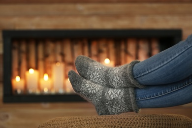 Photo of Woman wearing warm knitted socks near decorative fireplace indoors, closeup. Winter atmosphere