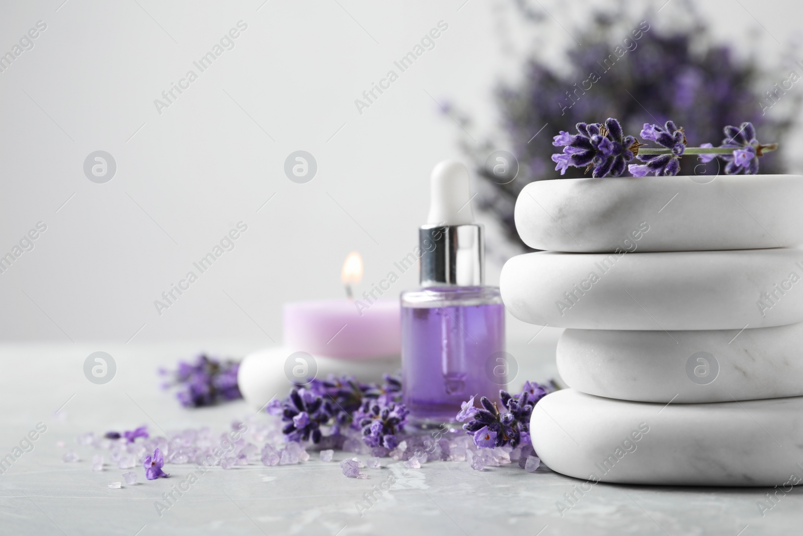 Photo of Spa stones, natural cosmetic oil and lavender flowers on grey table, space for text