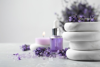 Photo of Spa stones, natural cosmetic oil and lavender flowers on grey table, space for text