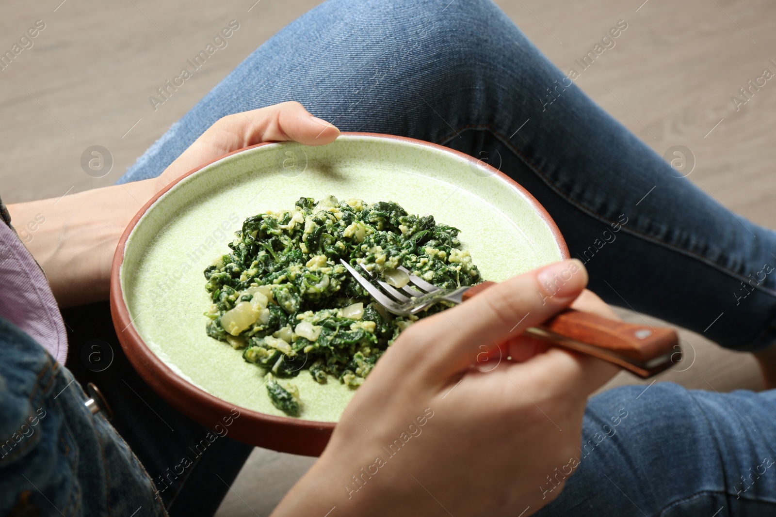 Photo of Young woman with plate of tasty spinach on wooden floor, closeup. Healthy food