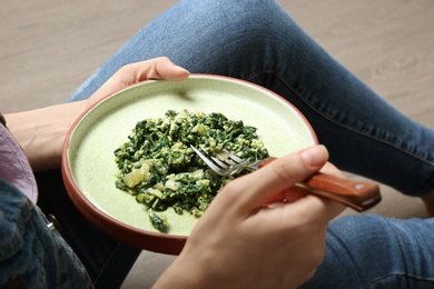 Photo of Young woman with plate of tasty spinach on wooden floor, closeup. Healthy food