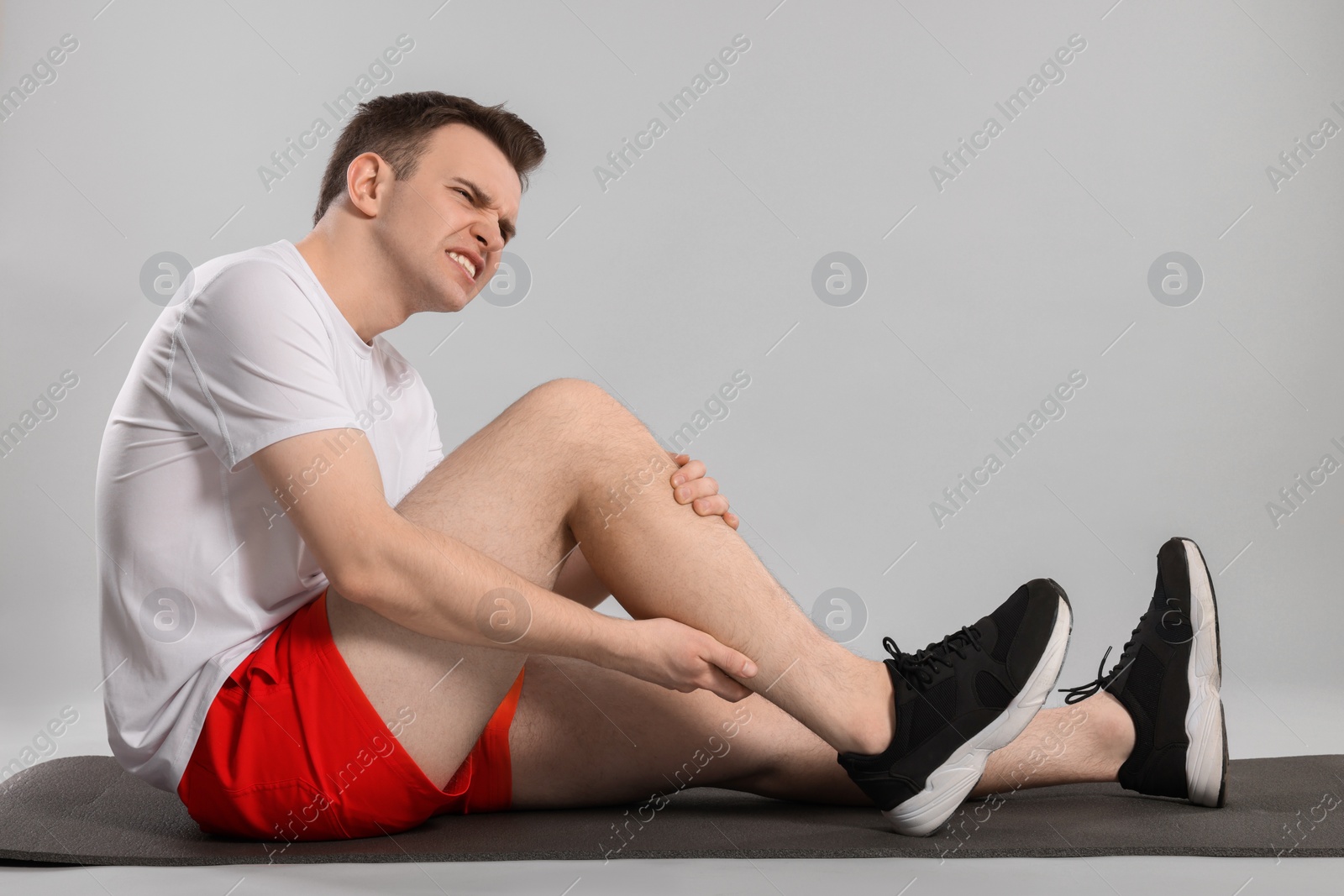 Photo of Man suffering from leg pain on mat against grey background