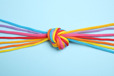 Photo of Colorful ropes tied together on light blue background, top view. Unity concept