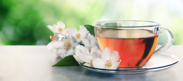 Cup of jasmine tea and fresh flowers on grey table outdoors, space for text. Banner design