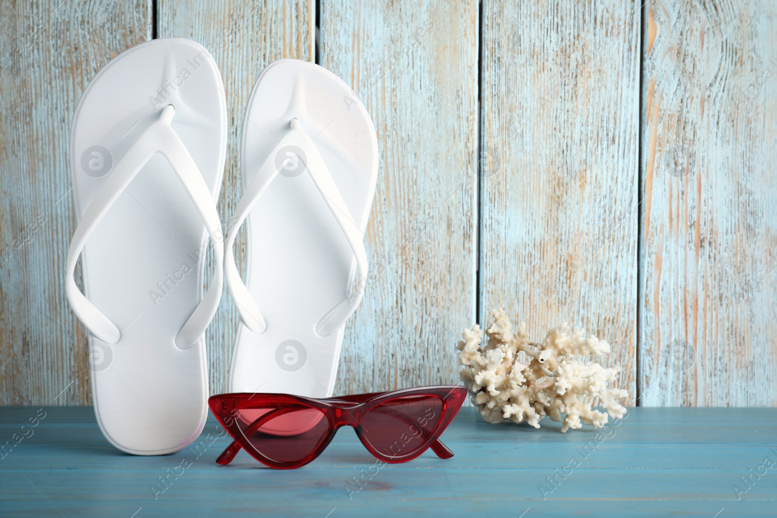 Photo of Stylish flip flops, coral and sunglasses near wooden wall