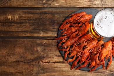 Delicious red boiled crayfishes and glass of beer on wooden table, top view. Space for text